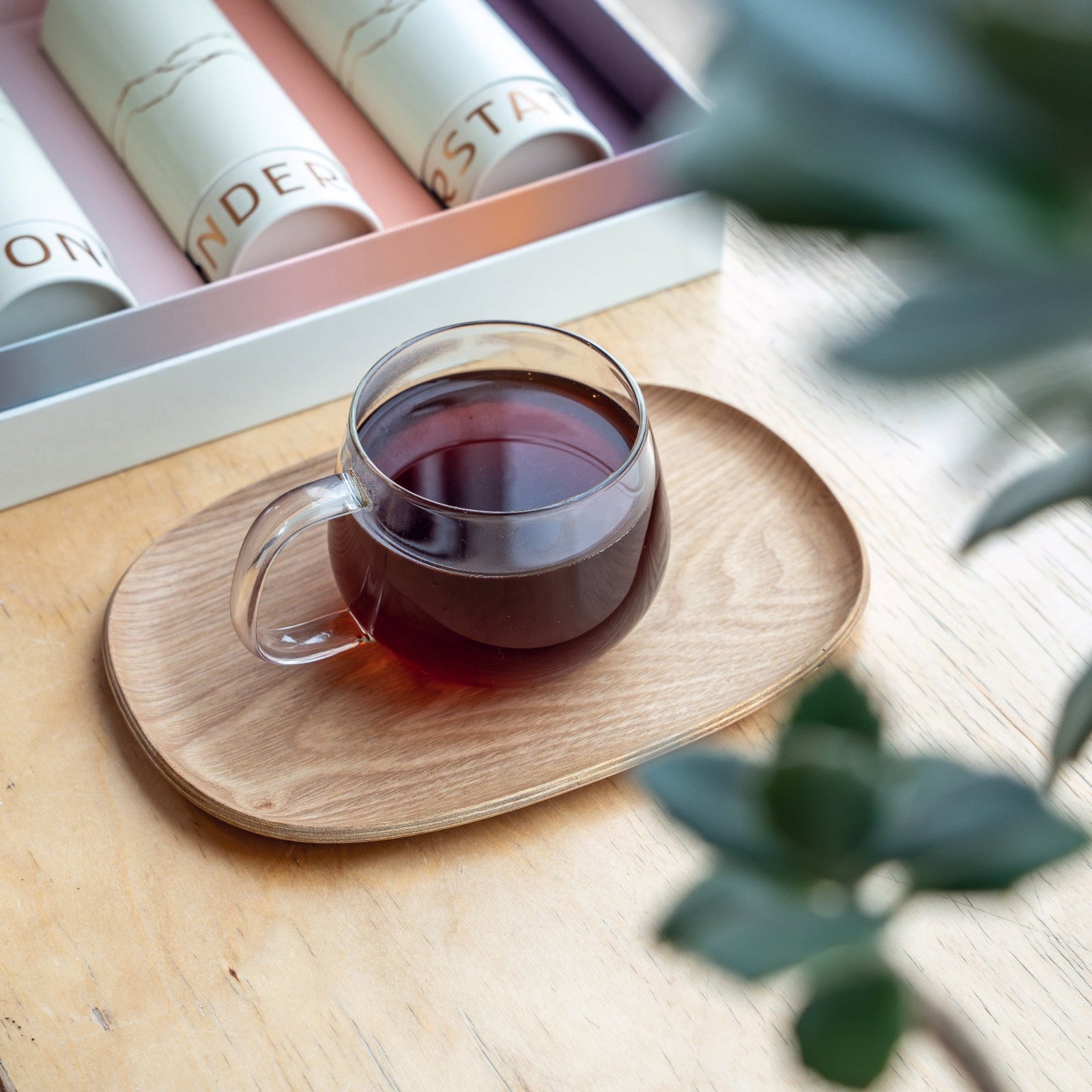 Clear glass mug filled with coffee on a wooden coaster, with stationery items in the background.